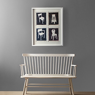 Une photographie de différentes chaises d’accent est accrochée au mur d’un vestibule au-dessus d’un banc à deux places.