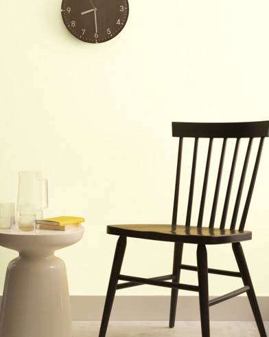 A brown clock hangs on a Crème Fraiche-painted wall above a dark wood chair and small dining table.
